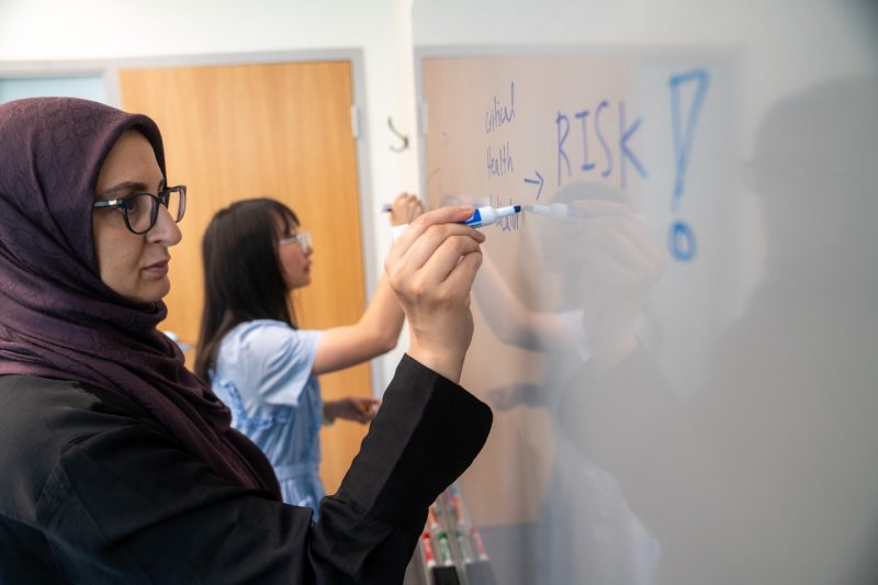 Hoda Eldardiry and Tong Wu sketch out an AI model at a whiteboard.